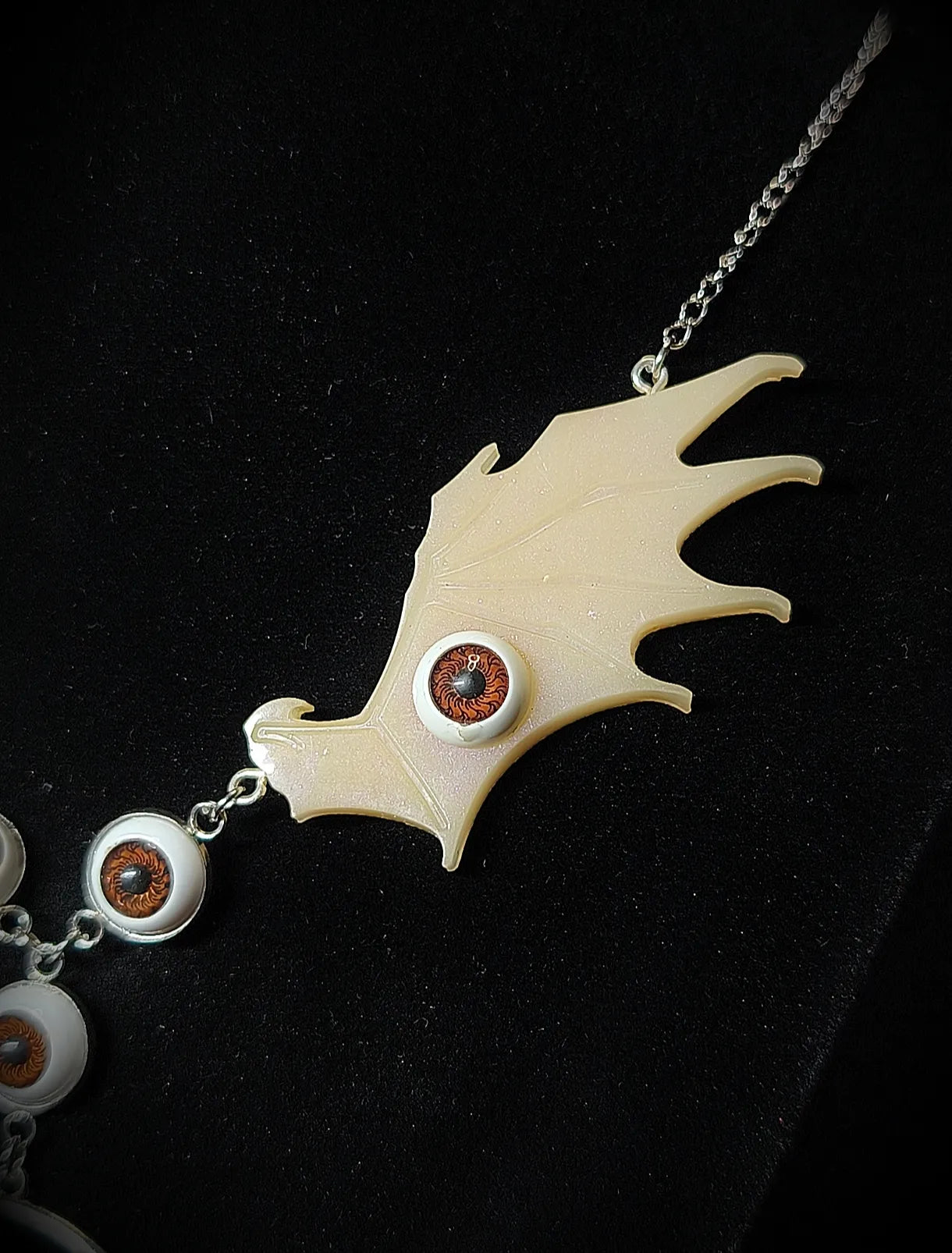 Détail aile ivoire ornée d'un œil sur collier gothique dark fantasy