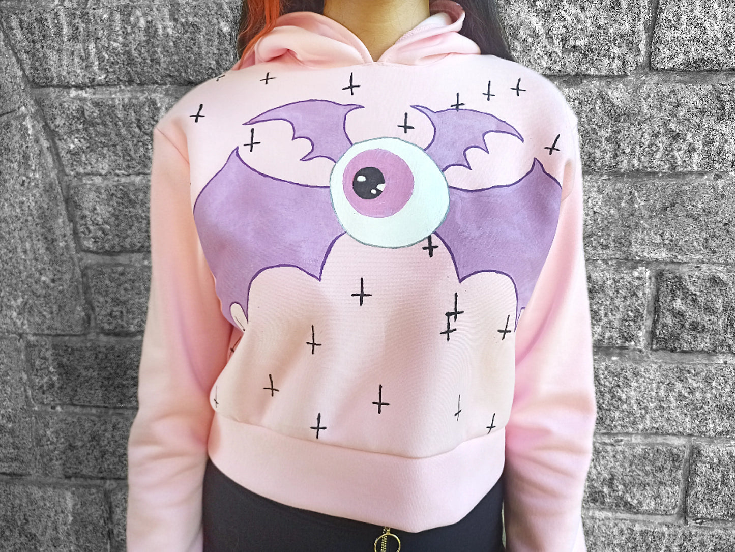 Détail de l'œil ailé et des croix noires sur sweat-shirt rose