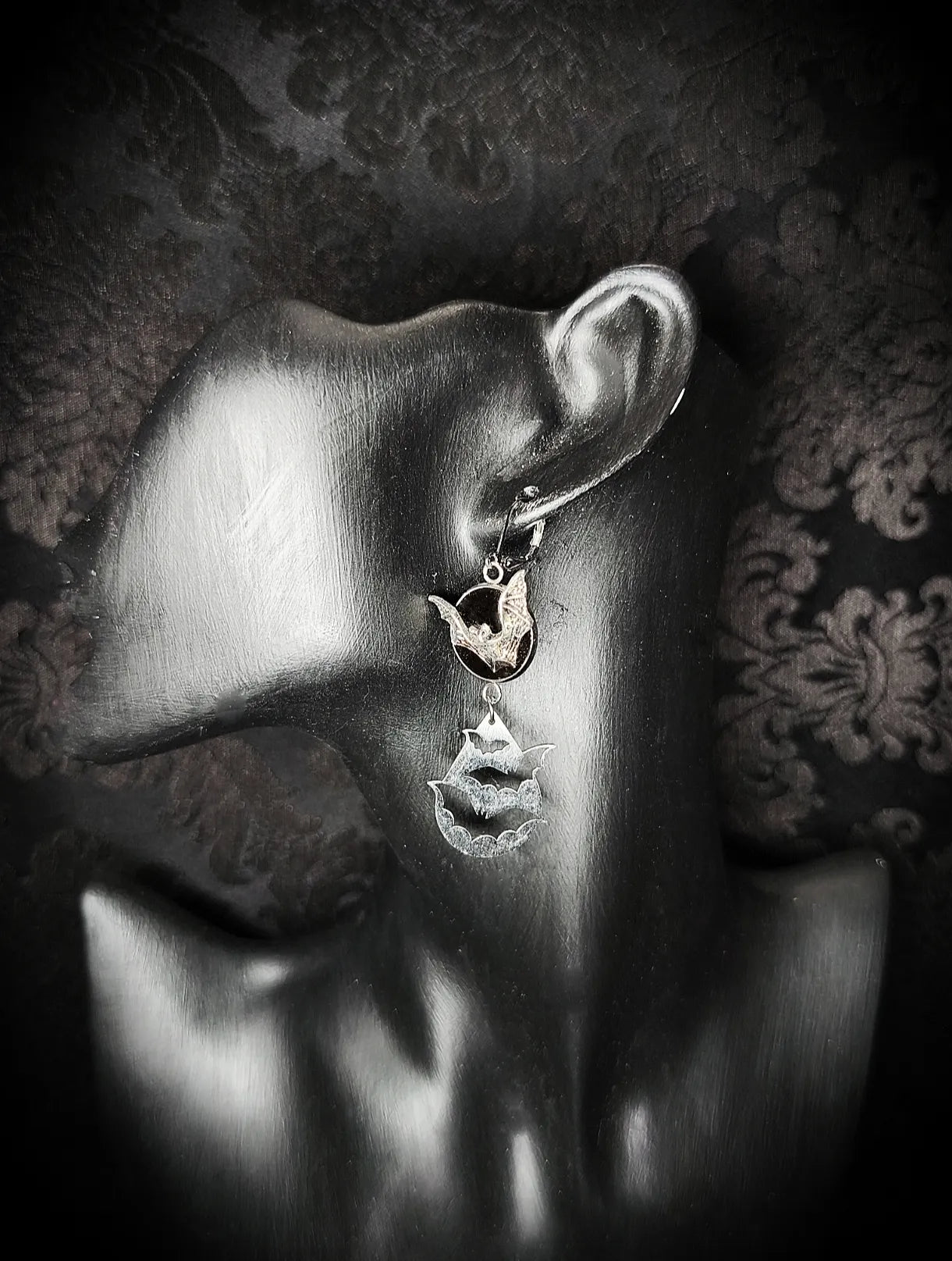 Boucle d’oreille gothique Vol Nocturne avec chauves-souris argentées et médaillon noir portée sur présentoir