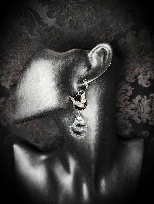 Boucle d’oreille gothique Vol Nocturne avec chauves-souris argentées et médaillon noir portée sur présentoir