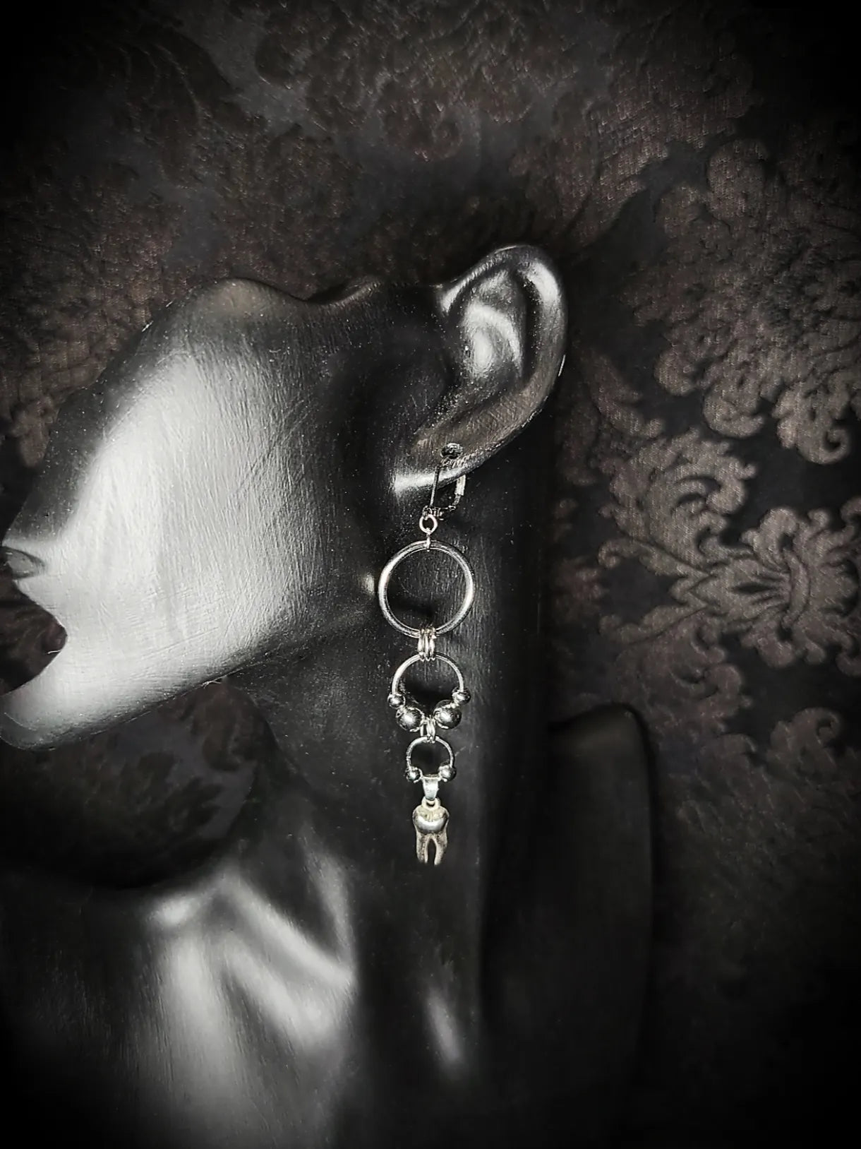 Boucle d’oreille gothique longue Morsure d’Acier avec anneaux argentés et pendentif dent sur présentoir noir