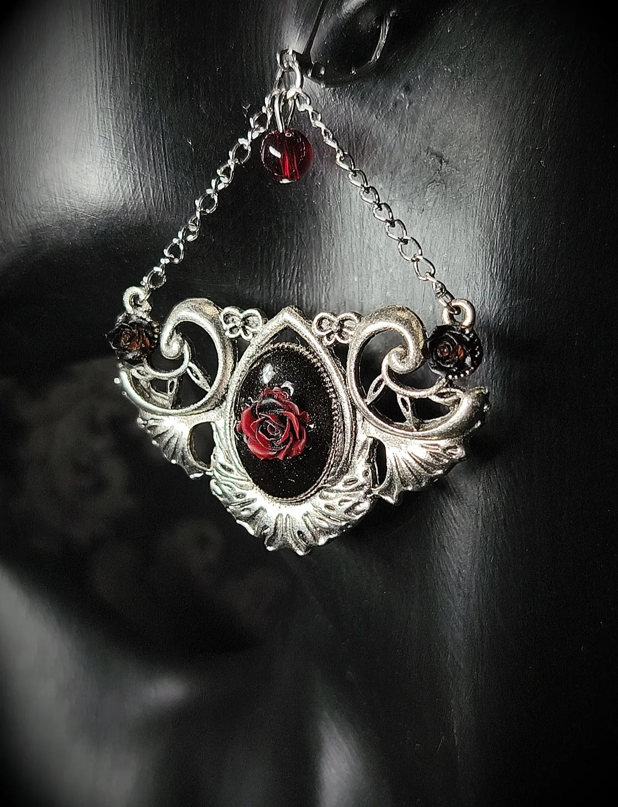 Détail du médaillon ornemental argenté avec rose rouge en résine UV de la boucle d’oreille Rosa Nocturna