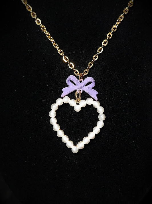 Gros plan du collier doré Cœur de Porcelaine avec cœur nacré et nœud violet pastel