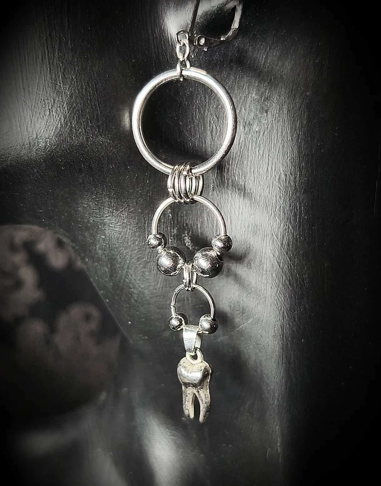 Vue rapprochée de la boucle d’oreille argentée composée d’anneaux et d’un pendentif en forme de dent