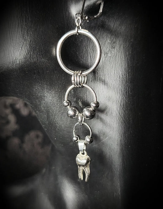 Vue rapprochée de la boucle d’oreille argentée composée d’anneaux et d’un pendentif en forme de dent
